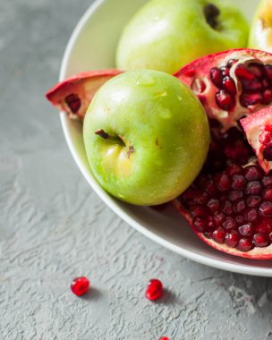 Taze elma ve nar bir beton zemin üzerine beyaz bir tabak içinde. Taze meyve. Natürmort