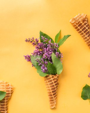 Dondurma külahı leylak dallarında parlak sarı bir arka plan ile. Taze çiçekler. güzel bir buket çiçek. Uzay kopyalayın. Metin için boş alan görüntüleyin. Metin için yer. Gıda fotoğraf. Düz yatıyordu, en iyi görünümü