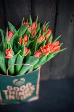 Bir kağıt torba koyu ahşap bir arka plan üzerinde kırmızı lale buketi. Bahar! Tazelik! Güzel bir buket çiçek. Metin için yer. Kartı orijinal arka plan veya kart. Vintage ülke rustik tarzı
