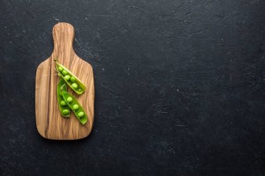 Young green peas on an olive wood board on a concrete black backgroundPlace for text. Flat lay, top view clipart