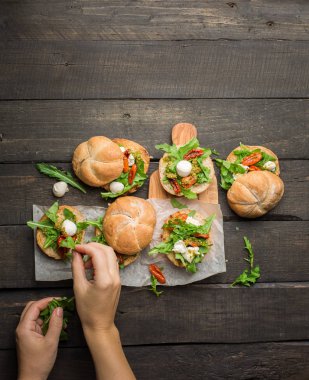 Roka, sandviçle kurutulmuş ev yapımı domates, pesto sos, mozzarella. Pişirme işlemi. Gıda Fotoğraf elleri olan. Atmosferik gıda fotoğraf ahşap koyu arka plan ile. Metin için yer. Düz yatıyordu, en iyi görünümü