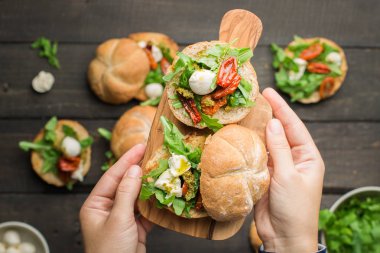 Roka, sandviçle kurutulmuş ev yapımı domates, pesto sos, mozzarella. Pişirme işlemi. Gıda Fotoğraf elleri olan. Atmosferik gıda fotoğraf ahşap koyu arka plan ile. Metin için yer. Düz yatıyordu, en iyi görünümü