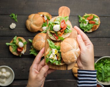 Roka, sandviçle kurutulmuş ev yapımı domates, pesto sos, mozzarella. Pişirme işlemi. Gıda Fotoğraf elleri olan. Atmosferik gıda fotoğraf ahşap koyu arka plan ile. Metin için yer. Düz yatıyordu, en iyi görünümü