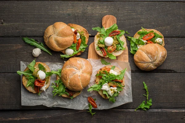 Roka, sandviçle kurutulmuş ev yapımı domates, pesto sos, mozzarella. Pişirme işlemi. Gıda Fotoğraf elleri olan. Atmosferik gıda fotoğraf ahşap koyu arka plan ile. Metin için yer. Düz yatıyordu, en iyi görünümü