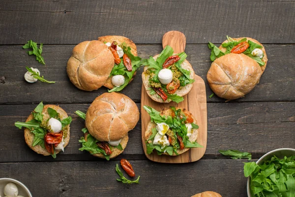 Roka, sandviçle kurutulmuş ev yapımı domates, pesto sos, mozzarella. Pişirme işlemi. Gıda Fotoğraf elleri olan. Atmosferik gıda fotoğraf ahşap koyu arka plan ile. Metin için yer. Düz yatıyordu, en iyi görünümü