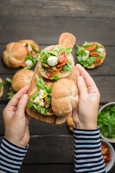 Roka, sandviçle kurutulmuş ev yapımı domates, pesto sos, mozzarella. Pişirme işlemi. Gıda Fotoğraf elleri olan. Atmosferik gıda fotoğraf ahşap koyu arka plan ile. Metin için yer. Düz yatıyordu, en iyi görünümü