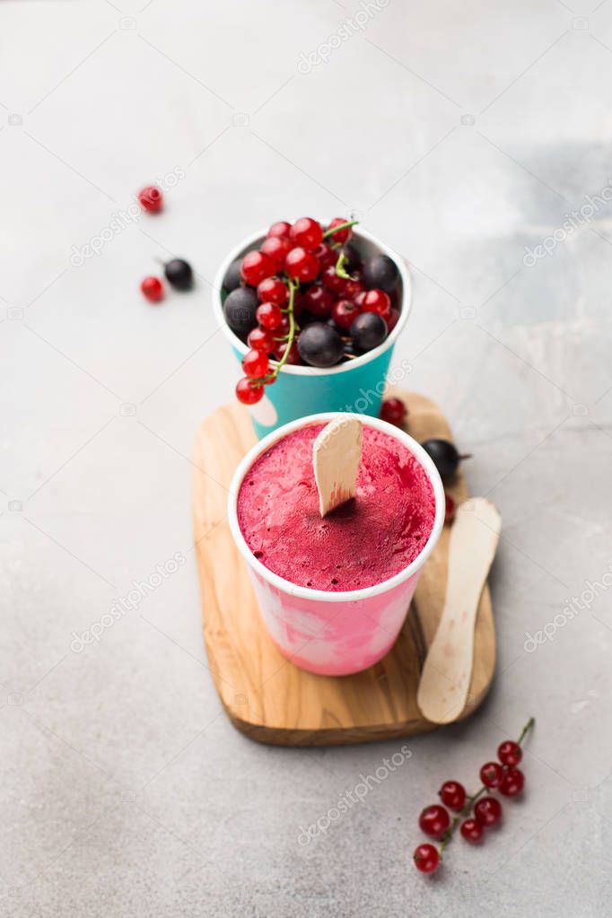 Frozen berry smoothies in bright paper cups on a light gray concrete background with fresh red currant and black gooseberry.place for text. flat lay, top view