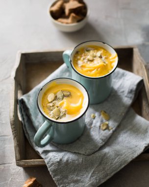 Balkabağı çorbası Hindistan cevizi sütü, kabak çekirdeği ve gri beton zemin üzerine vintage mavi bardağı içinde baharatlar ile. Atmosferik karanlık gıda fotoğraf. 