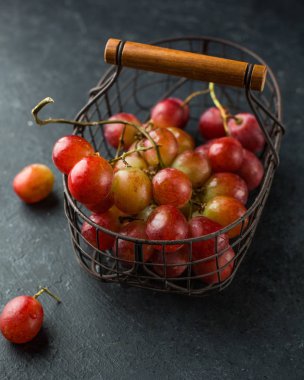 Dal siyah bir beton zemin üzerine vintage demir sepet içinde kırmızı büyük üzüm. Taze meyve, güzel kart ya da geçmişi