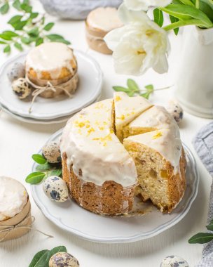 Hafif ahşap arka plan üzerinde geleneksel Paskalya kek. Çiçeklerle süslenmiş. Yanındaki küçük bir pasta, bıldırcın yumurtası ve çiçekler. Bir parça kek kes. Paskalya. Kutlama. Bahar. Rustik tarzı