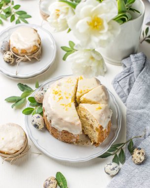 Hafif ahşap arka plan üzerinde geleneksel Paskalya kek. Çiçeklerle süslenmiş. Yanındaki küçük bir pasta, bıldırcın yumurtası ve çiçekler. Bir parça kek kes. Paskalya. Kutlama. Bahar. Rustik tarzı