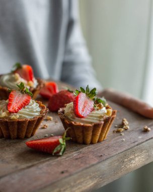 Mini tartlets peynirli kremalı ve taze çilek, bir ahşap kutu fındık serpilir. Elleri ile gıda fotoğraf.