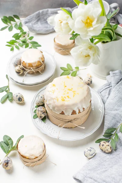 Hafif ahşap arka plan üzerinde geleneksel Paskalya kek. Çiçeklerle süslenmiş. Yanındaki küçük bir pasta, bıldırcın yumurtası ve çiçekler. Bir parça kek kes. Paskalya. Kutlama. Bahar. Rustik tarzı