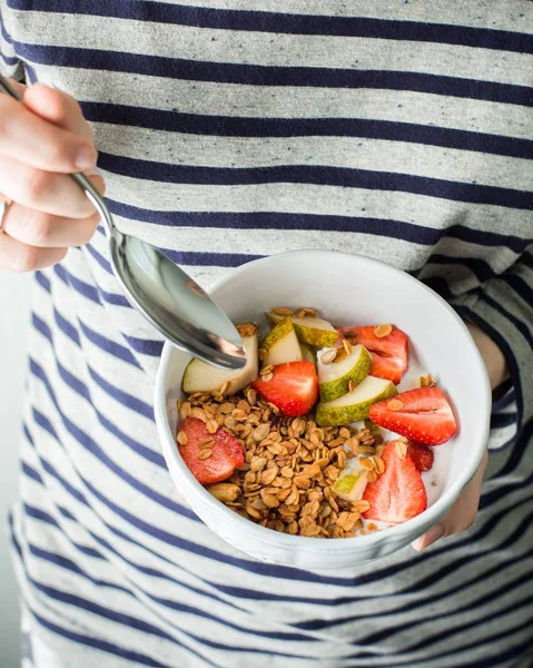 Homemade granola with fresh strawberries and pears. Food photo with hands. Hercules flakes (oat flakes), sunflower seeds, fresh peanuts, hazelnuts, honey. Useful breakfast.