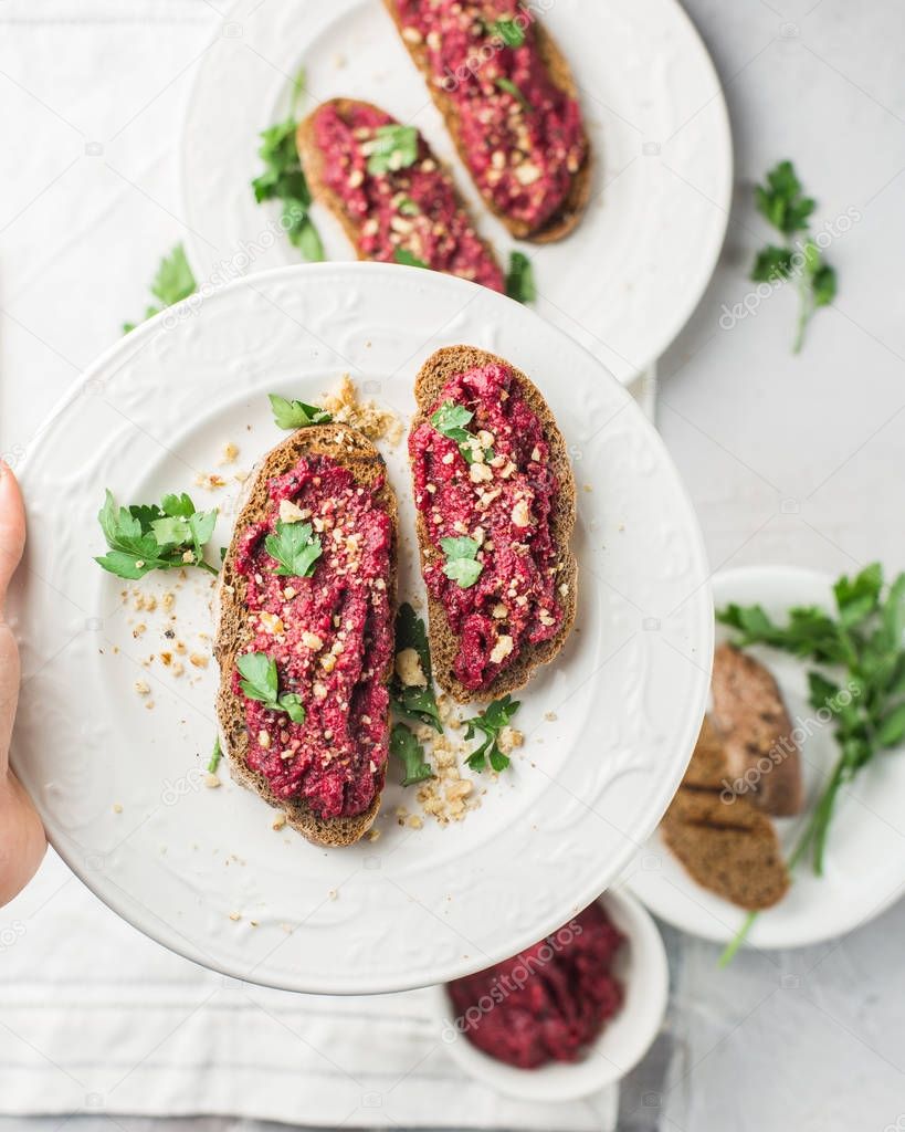 Homemade toast from whole grain bread with beet paste, greens and nuts. Light concrete background, white soft. Place for text. Food photo with hands. Useful dietary baking. Flat lay, top view