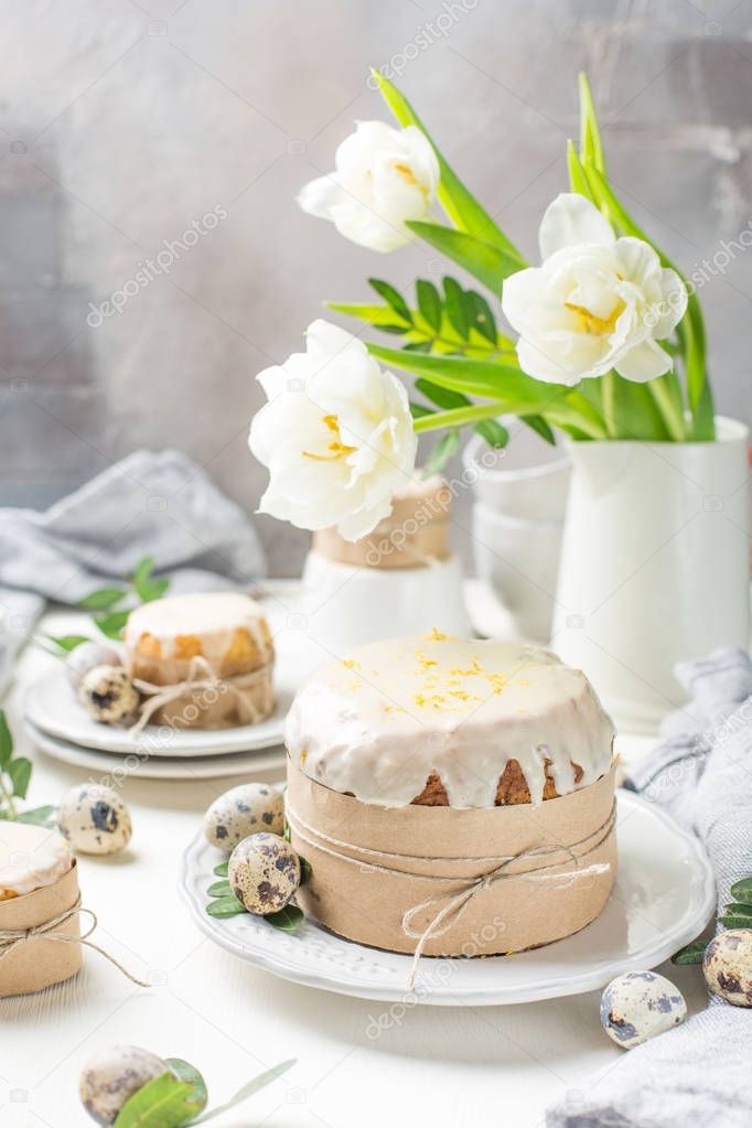 Traditional Easter cake on a light wooden background. Decorated with flowers. Next to a small cake, quail eggs and flowers. Cut a piece of cake. Easter. Celebration. Spring. Rustic style