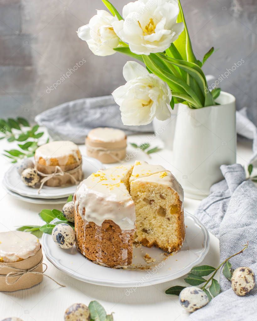 Traditional Easter cake on a light wooden background. Decorated with flowers. Next to a small cake, quail eggs and flowers. Cut a piece of cake. Easter. Celebration. Spring. Rustic style