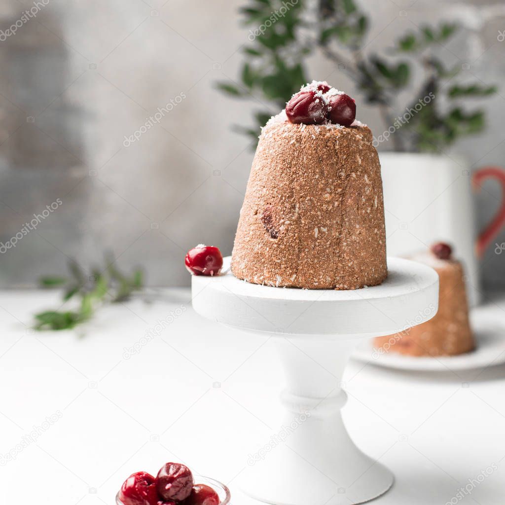 Chocolate mini raw cake with cherry and cottage cheese, decorated with cherries and coconut. Traditional Russian Easter dessert. On a light white wooden background. Piece of cake.