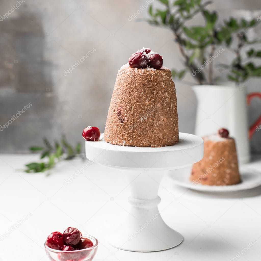 Chocolate mini raw cake with cherry and cottage cheese, decorated with cherries and coconut. Traditional Russian Easter dessert. On a light white wooden background. Piece of cake.