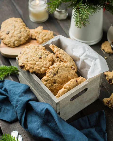 The perfect tasty breakfast. Oatmeal cookies with chocolate in wooden box and green tea with lemon in mugs on a dark background with a Xmas tree. Best useful Cookies.