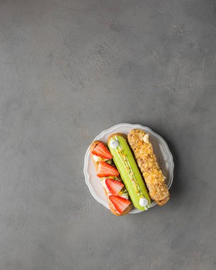 Beyaz tabakta taze çilek, vanilya kreması, fındık ve şam fıstıklı badem kurabiyesi ile Fransız choux hamur işi (eclairs). Boş arkaplan çok güzel. Restoran konsepti. Düz yatıyordu