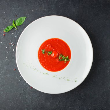 Baharatlı domates çorbası ve siyah beton arka planda beyaz bir tabakta taze fesleğen. Faydalı bir beslenme ve öğle yemeği. Mesaj için yer. Düz yerde, üst tarafta. İzole edilmiş.