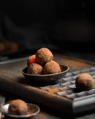 Çikolatalı trüf. Koyu renkli ahşap bir arka planda kakao serpiştirilmiş koyu çikolata ve vişne şekeri. Atmosferik yemek fotoğrafı. Ev yapımı taze enerji topları..