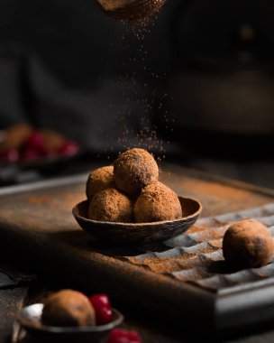 Çikolatalı trüf. Koyu renkli ahşap bir arka planda kakao serpiştirilmiş koyu çikolata ve vişne şekeri. Atmosferik yemek fotoğrafı. Ev yapımı taze enerji topları..
