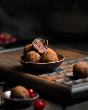 Çikolatalı trüf. Koyu renkli ahşap bir arka planda kakao serpiştirilmiş koyu çikolata ve vişne şekeri. Atmosferik yemek fotoğrafı. Ev yapımı taze enerji topları..