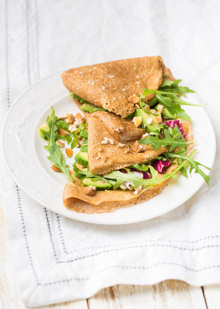 English-style (or Russian -style) useful whole grained pancakes with avocado, radicchio, arugula and almonds on a light wooden background.Useful dietary snack.