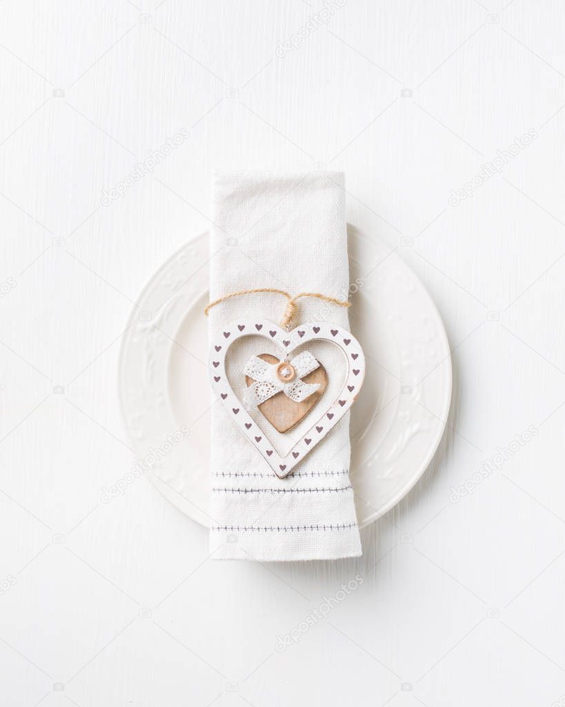 Valentines day meal background with white wood vintage heart, white plate and napkin. Romantic holiday table setting. Beautiful background with blank. Restaurant concept.Flat lay