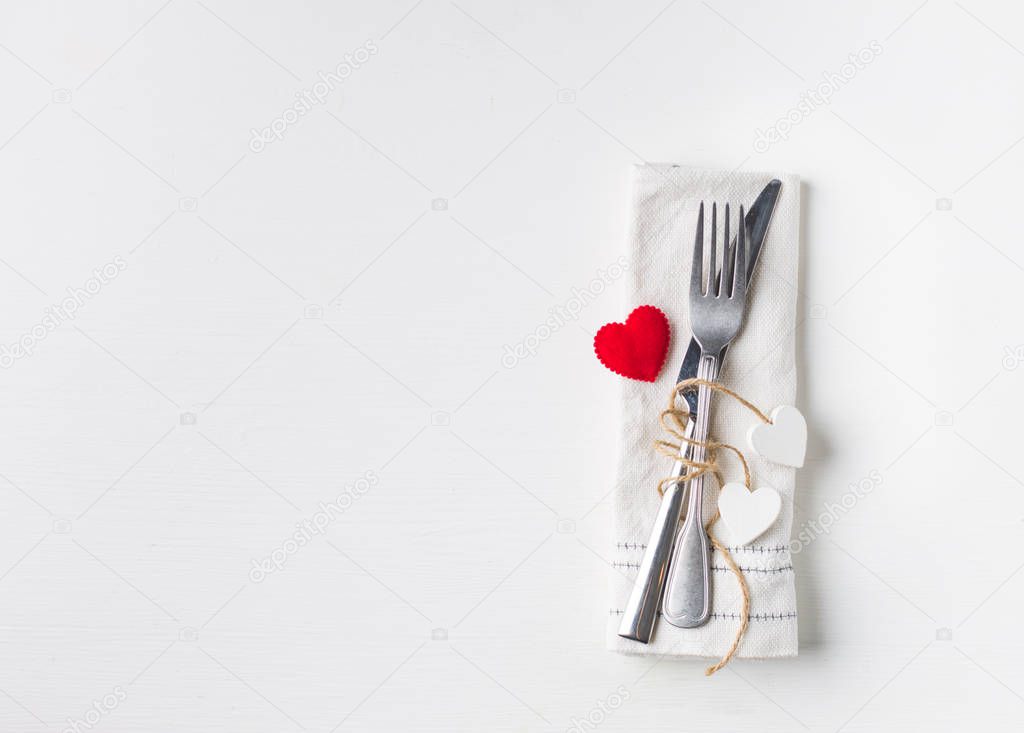 Valentines day (or wedding) meal background with red ribbon, hearts, fork, knife, white plate and napkin. Romantic holiday table setting. Beautiful background with blank. Restaurant concept. Flat lay