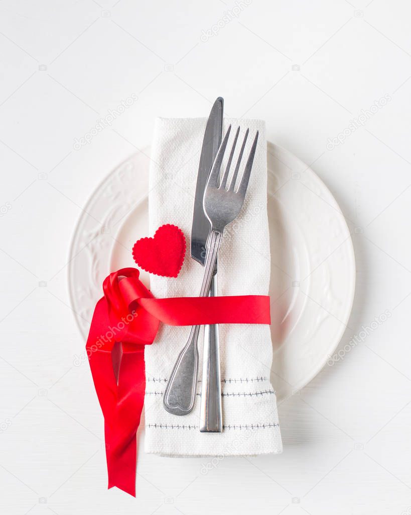 Valentines day (or wedding) meal background with red ribbon, hearts, fork, knife, white plate and napkin. Romantic holiday table setting. Beautiful background with blank. Restaurant concept. Flat lay