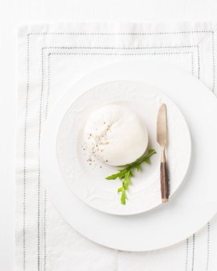 İtalyan peynirli Burrata (mozzarella) taze roka, domates, zeytin yağı, sos pesto ve tahıllı ekmeği beyaz bir tabakta ve ahşap arkaplanda kızartıyorlar.