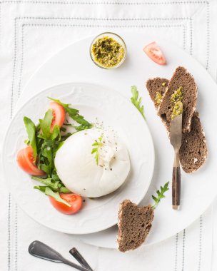 İtalyan peyniri dilimlenir Burrata (mozzarella) taze roka, domates, zeytin yağı, sosu pesto ve tam tahıllı ekmek tost beyaz bir tabak ve ahşap açık renkli. Düz yatıyordu, en iyi görünümü