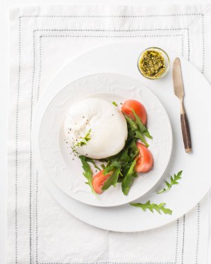 İtalyan peyniri dilimlenir Burrata (mozzarella) taze roka, domates, zeytin yağı, sosu pesto ve tam tahıllı ekmek tost beyaz bir tabak ve ahşap açık renkli. Düz yatıyordu, en iyi görünümü