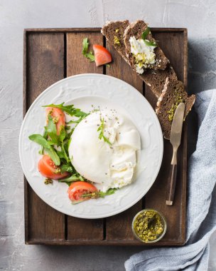 İtalyan peynir Burrata vintage bir bıçak, taze roka, domates, zeytin yağı ile dilimlenmiş, pesto sos ve bütün tahıl tost bir ahşap kutu ve hafif beton bir arka plan üzerinde ekmek. Mmm, lezzetli.) Düz yatıyordu