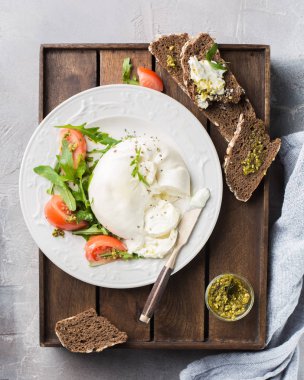 İtalyan peynir Burrata vintage bir bıçak, taze roka, domates, zeytin yağı ile dilimlenmiş, pesto sos ve bütün tahıl tost bir ahşap kutu ve hafif beton bir arka plan üzerinde ekmek. Mmm, lezzetli.) Düz yatıyordu