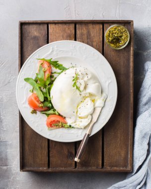 İtalyan peynir Burrata vintage bir bıçak, taze roka, domates, zeytin yağı ile dilimlenmiş, pesto sos ve bütün tahıl tost bir ahşap kutu ve hafif beton bir arka plan üzerinde ekmek. Mmm, lezzetli.) Düz yatıyordu