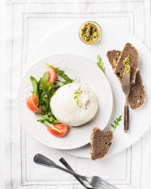İtalyan peyniri dilimlenir Burrata (mozzarella) taze roka, domates, zeytin yağı, sosu pesto ve tam tahıllı ekmek tost beyaz bir tabak ve ahşap açık renkli. Düz yatıyordu, en iyi görünümü