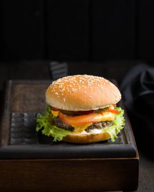 Sığır eti, domates, peynir ve marul, kızarmış patates ve bira ile lezzetli taze lezzetli burger ahşap kesme tahtası koyu arka plan üzerinde servis. Sokak lokanta