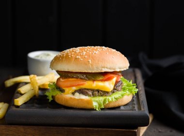 Sığır eti, domates, peynir ve marul, kızarmış patates ve bira ile lezzetli taze lezzetli burger ahşap kesme tahtası koyu arka plan üzerinde servis. Sokak lokanta