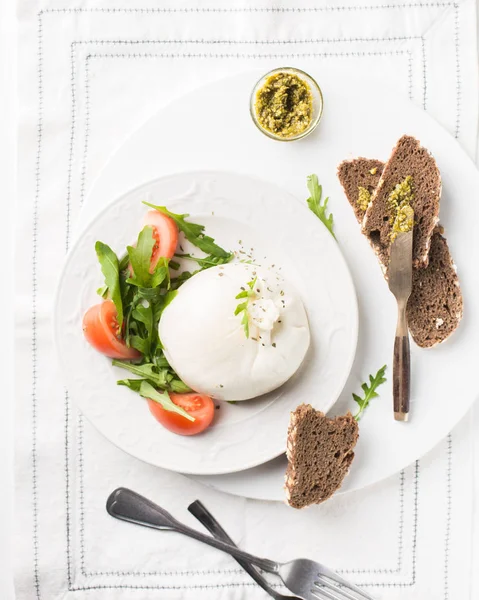 İtalyan peyniri dilimlenir Burrata (mozzarella) taze roka, domates, zeytin yağı, sosu pesto ve tam tahıllı ekmek tost beyaz bir tabak ve ahşap açık renkli. Düz yatıyordu, en iyi görünümü