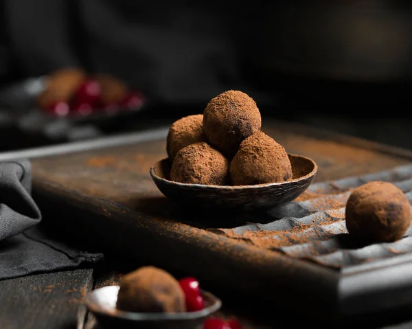 Çikolata. Çikolata ve vişneli şeker koyu, rustik tarzda koyu ahşap zemin üzerine kakao serpilir. Atmosferik gıda fotoğraf. Ev yapımı taze enerji topları.