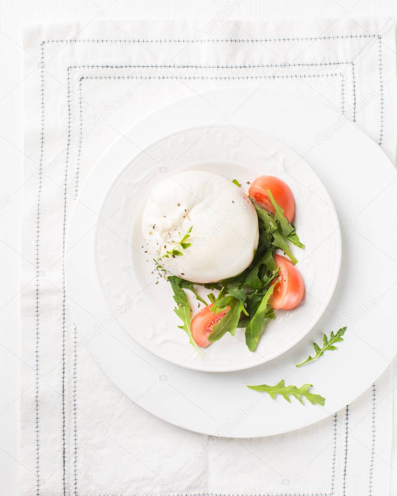 Italian cheese Burrata (mozzarella) with fresh arugula, tomatoes, olive oil, sauce pesto and whole grain bread toasts on a white plate and a wooden light background.Flat lay, top view