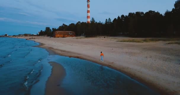 Одинока дівчина йде на пляжі біля Північного моря. Похмуре небо і холодна блакитна атмосфера. Озеро Місті в старовинному скандинавському стилі. Ладога в Ленінградській області, Росія. Вид з повітря на морський мис. 4k польоту — стокове відео