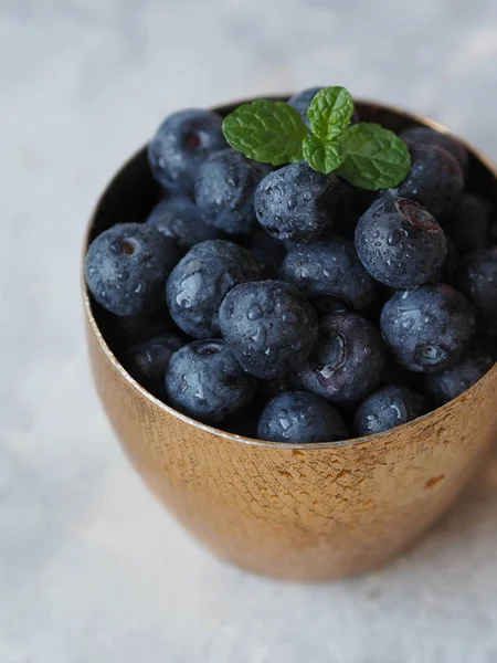 Ripe wet blueberries and a sprig of mint  in a golden glass — Stock Photo, Image