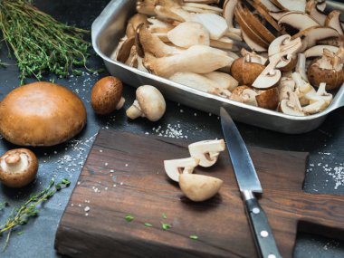 Bir kesme tahtası ve otlar ile karanlık bir tabloda çeşitli ham mantar. Seçici odak. 