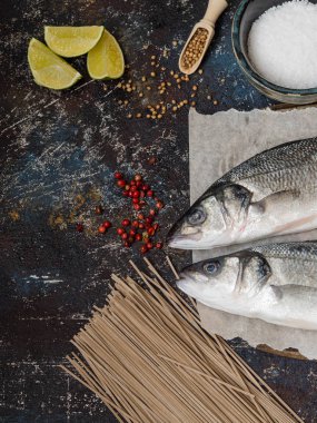 İki çiğ balık deniz levreği ve diğer malzemelerin vintage koyu arka plan üzerine