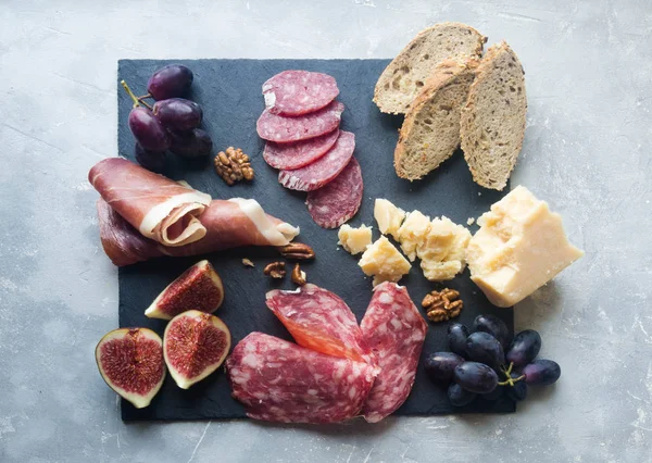 Çeşitli et, peynir, üzüm, ekmek ve incir gri bir arka plan üzerinde koyu yönetim kurulu